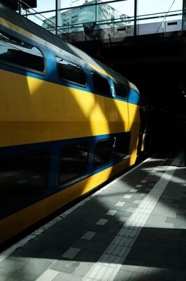Tweede klas trein met gele en blauwe kleuren in een station, met schaduwen van licht op de vloer.