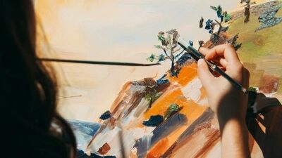 Een hand schildert een kleurrijk landschap met bomen en een zee op een canvas.