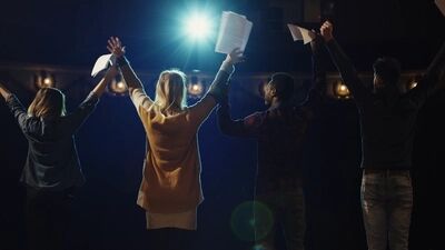 Groep mensen met opgestoken armen en scripts in handen, tegen een achtergrond met een blauwe lichtstraal.