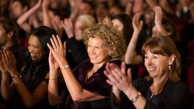 Een applaudiserend publiek van vrouwen in een theater, met blije gezichten en veel handgeklap.