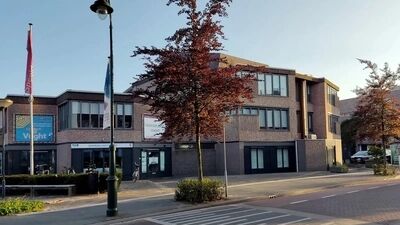 Moderne gevel van een gebouw met bomen en een parkeerplaats in een stedelijke omgeving onder een blauwe lucht.