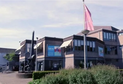 Een moderne gebouw met grote ramen, omgeven door flaggen en plantenbedden.